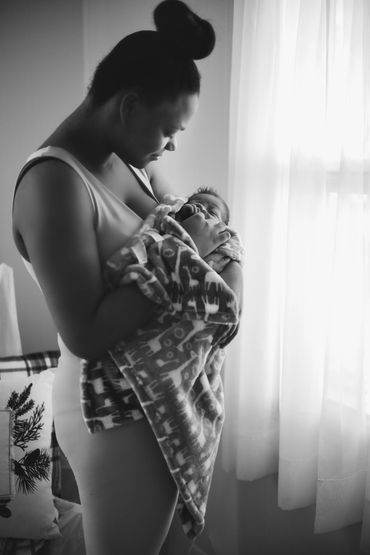 A mother standing by a window, holding her newborn during a lifestyle newborn photo session, 