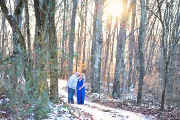 Photo of a couple standing in the woods with a snow covered ground for a maternity photo session