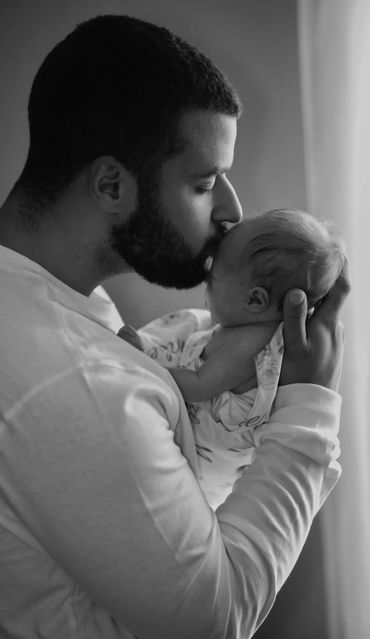 black & white photo of father holding newborn close and kissing on forehead.