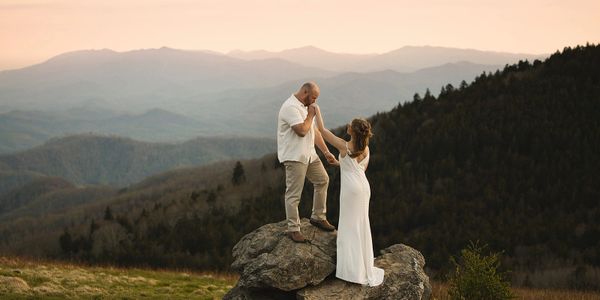 Groom kissing his bride's hand atop a boulder at sunset during their Roan Mountain elopement at Carv