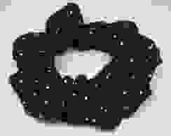 A black handmade scrunchie with white dots placed on an all white background.