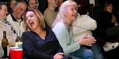 Two women laughing joyfully in a lively social gathering.