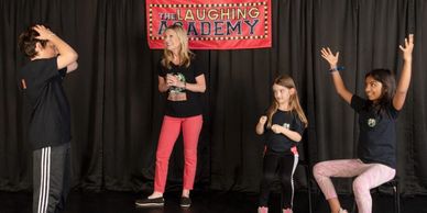 Three children and a woman engage in a fun acting class at The Laughing Academy.