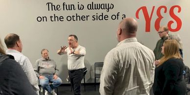 A man leading a group discussion in front of a motivational wall quote.