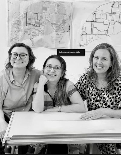 Three women smiling at a table with maps on the wall behind them.