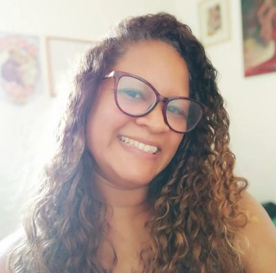 Smiling woman with curly hair and glasses in a cozy room.
