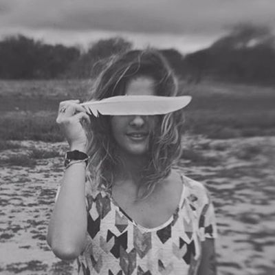 Woman holding a feather over her eyes in a serene outdoor setting.
