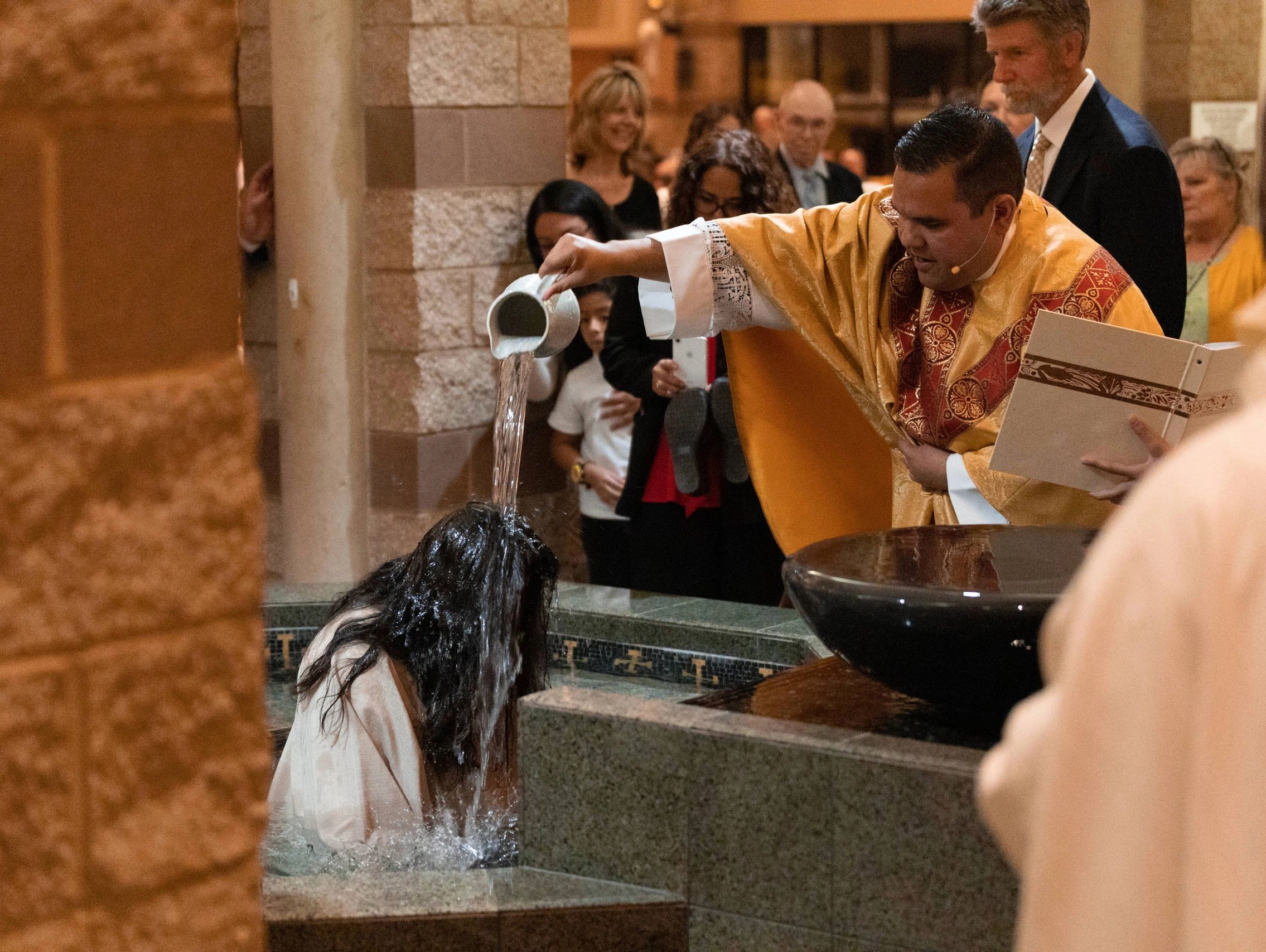 A priest baptizes a woman by pouring water over her head in a church ceremony.