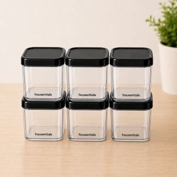 Six clear square containers with black lids on a wooden surface.
