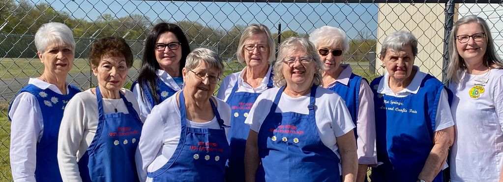 Group of smiling women standing outside wearing white shirts with blue aprons