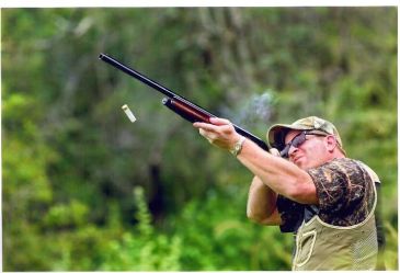 Man shooting a shotgun outdoors.