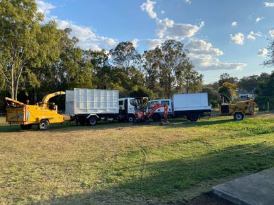 Two trucks and machinery parked on grassy field under blue sky.