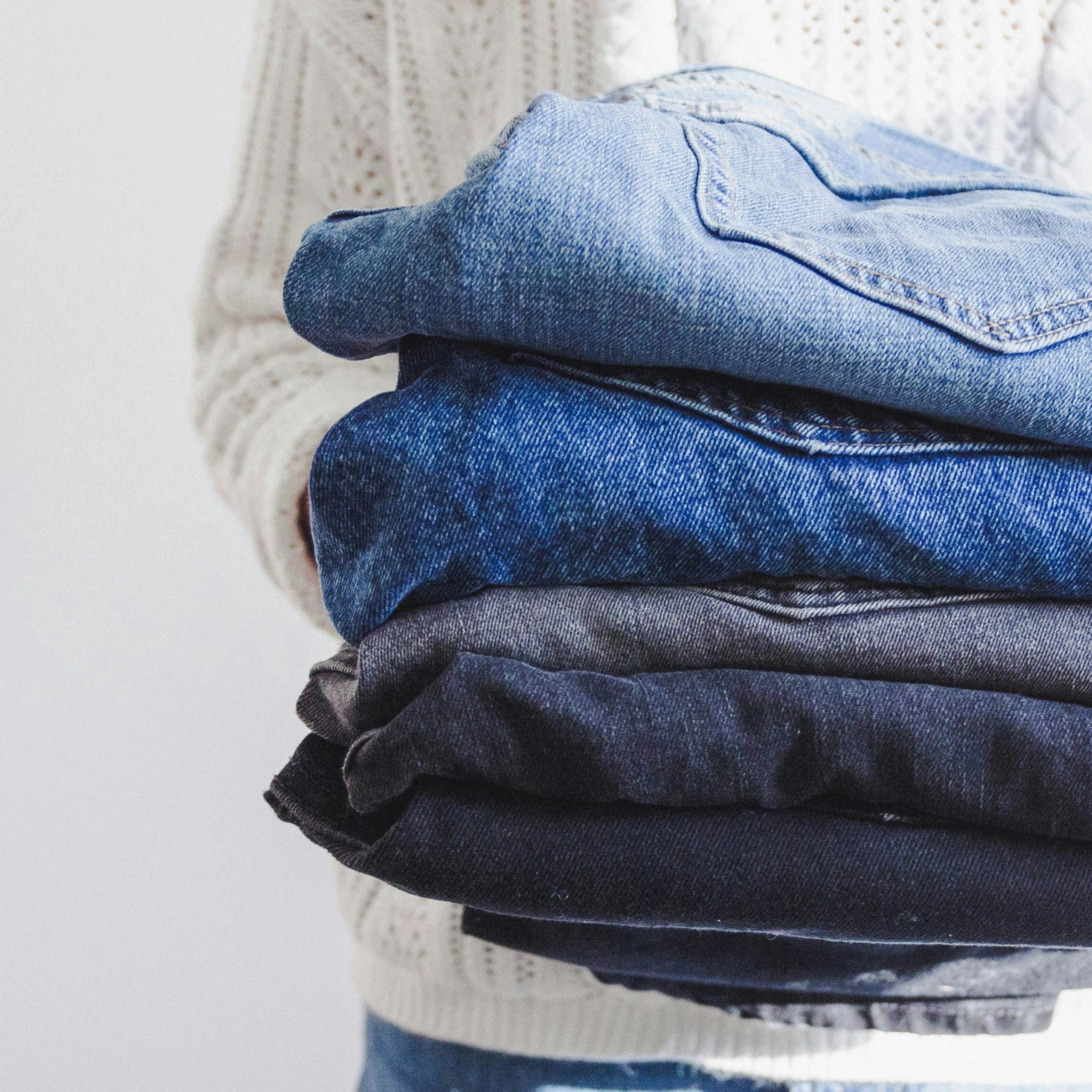 Person holding a stack of folded denim jeans in various shades.