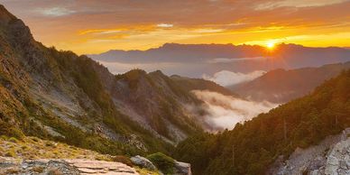 Sunrise over misty mountain valleys with rocky slopes and forests.