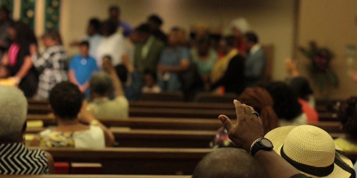 Congregation members seated in church pews, one person raising a hand.
