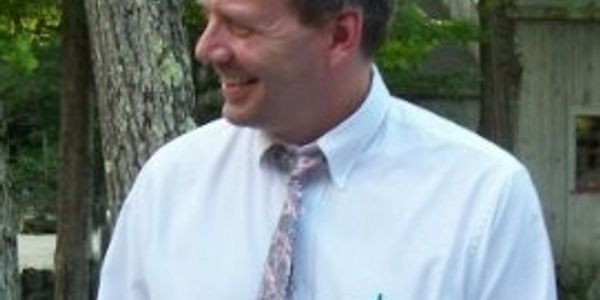 Smiling man in white shirt and tie outdoors.