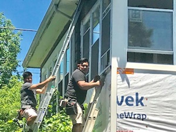 Two workers on ladders installing siding on a house exterior.