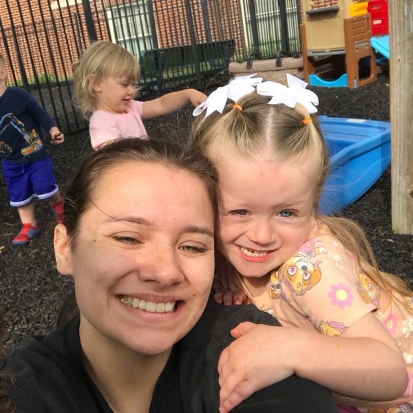 A smiling woman with a young girl hugging outdoors at a playground.