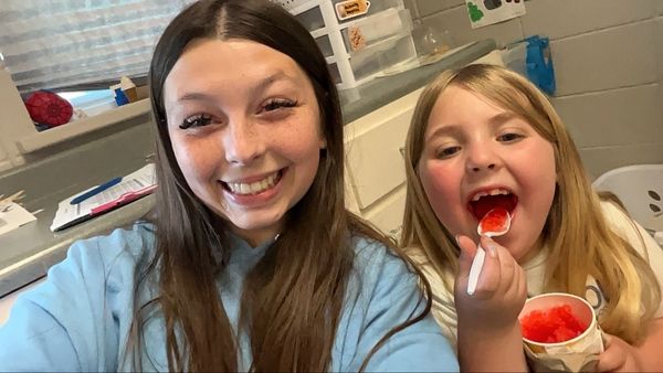 Two girls smiling, one eating red shaved ice.