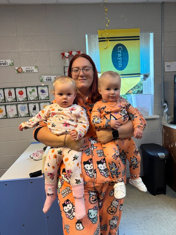Woman holding two babies, all dressed in Halloween-themed pajamas.