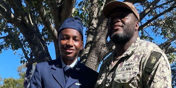 Two military personnel posing outdoors under a tree.