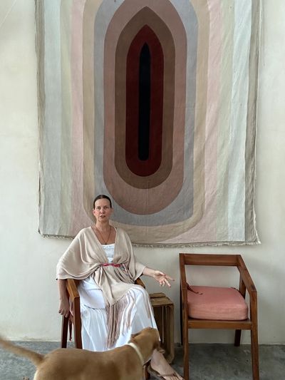 Woman sitting on a chair with a large abstract wall hanging behind her and a dog in the foreground.