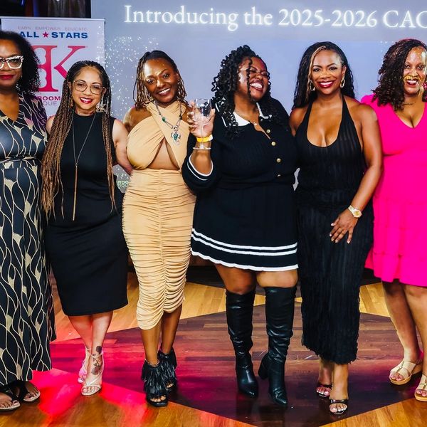 Group of six stylish women posing and smiling at an event.