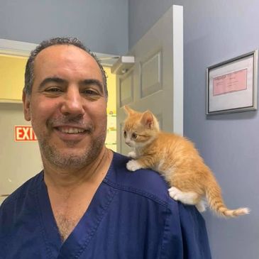 Man smiling with an orange kitten on his shoulder.