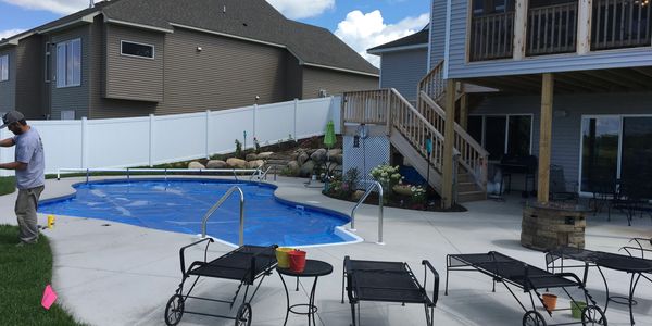 Concrete Pool Deck With A Blue Oval Pool, Lounge Chairs, And Fire Pit.