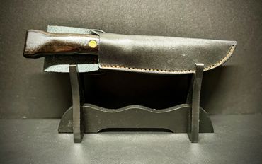 A knife with a wooden handle in a black leather sheath on a black stand.