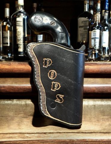 A vintage gun holster labeled 'POPS' on a wooden bar counter.