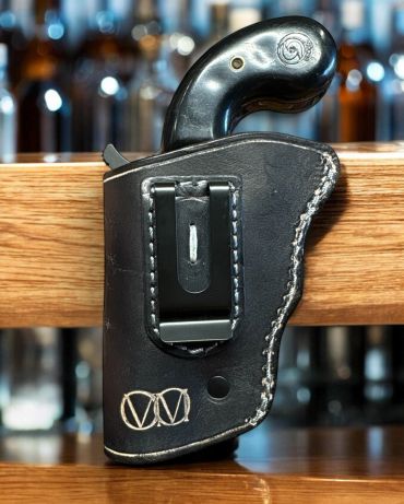 Black pistol in a stitched leather holster with a belt clip.