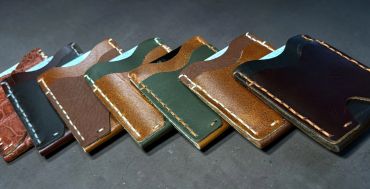 A row of handcrafted leather wallets in various colors and stitches.