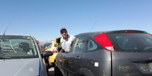 Man smiling between parked cars in a lot.