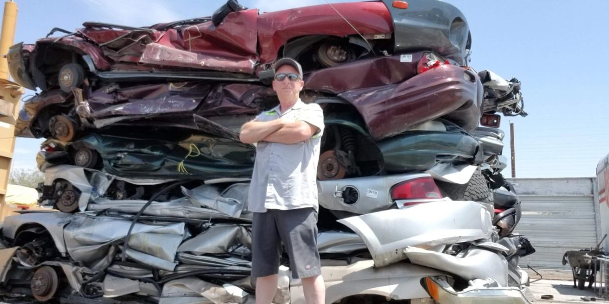 Man stands confidently in front of stacked crushed cars.