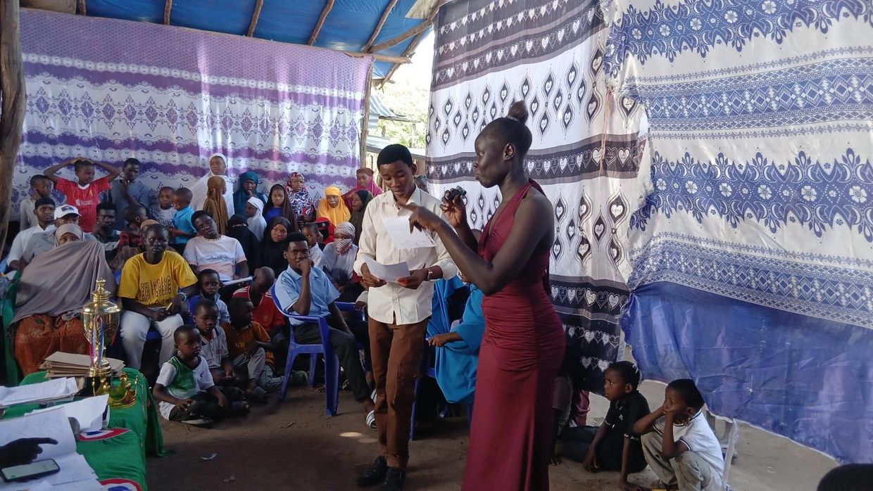 A woman in a red dress speaks to a crowd gathered in a decorated tent.