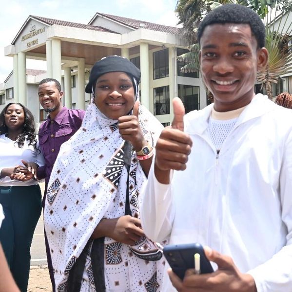 Happy group of young people outside a building, thumbs up and smiling.