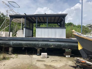 Large pontoon boat on dry land with a small structure on top.