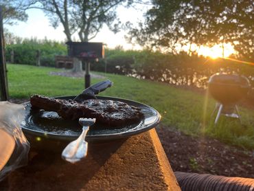 Grilled steak on a plate with a fork at sunset.