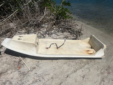 Old white paddle boat on sandy shore.