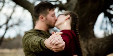 A couple kissing showing off the engagement ring while dancing.