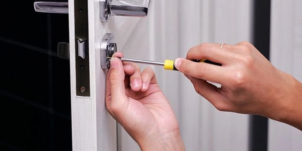 Hands using a screwdriver to fix a door lock.