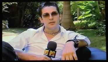 Young man in sunglasses being interviewed outdoors holding an MTV microphone.