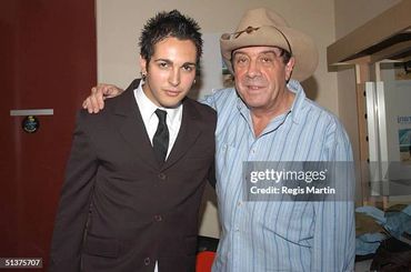 Two men posing together indoors, one in a suit and the other in a cowboy hat.