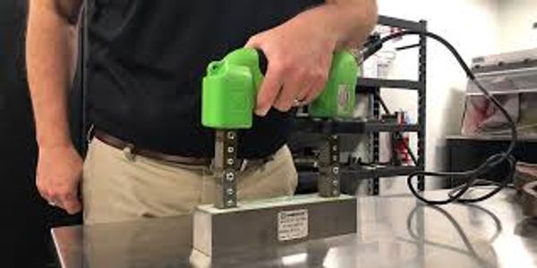 Person using a green handheld device on a metal block in a workshop.