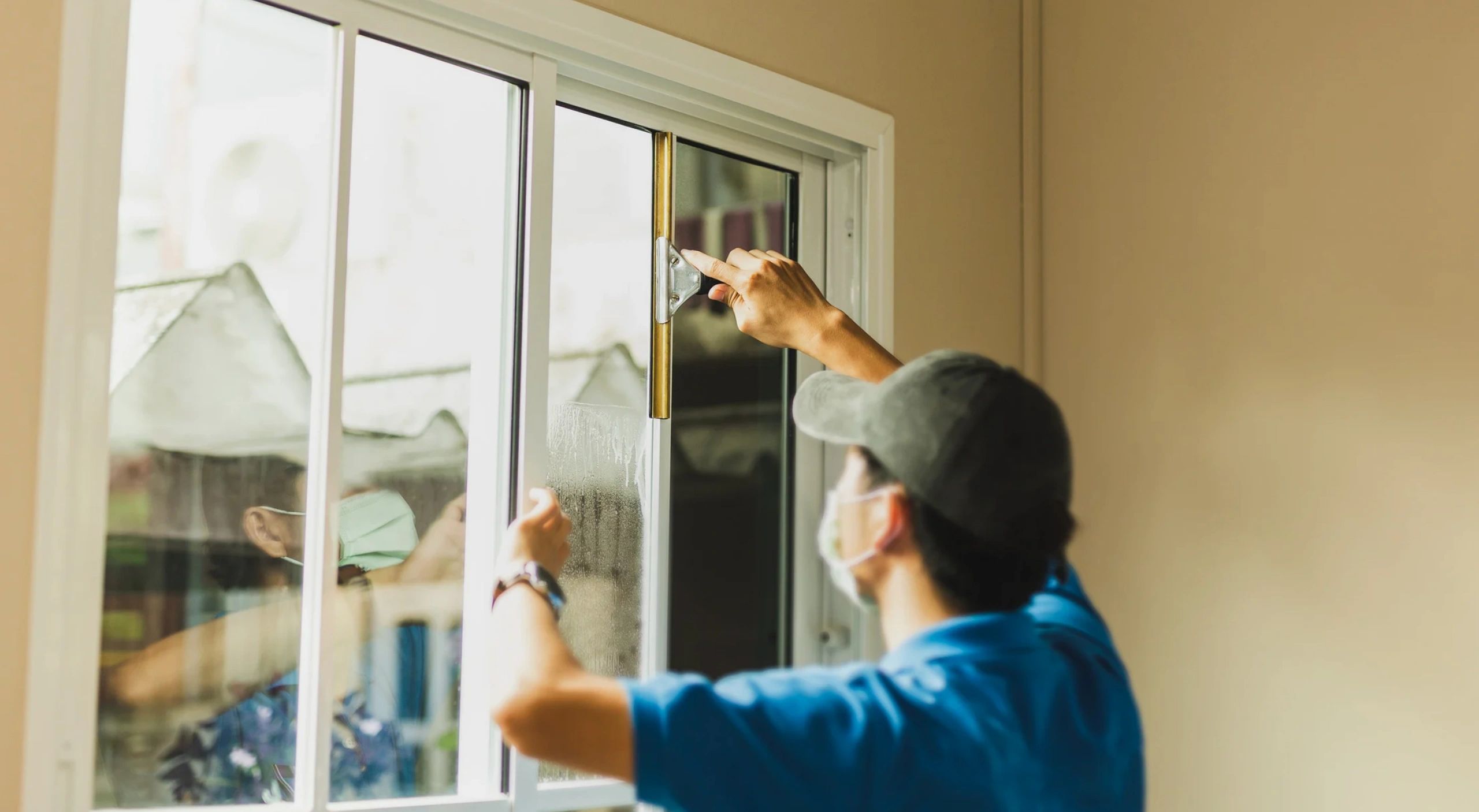 A person wearing a mask opening a sliding glass window indoors.