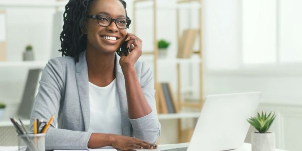 Smiling woman talking on phone at her desk with laptop and stationery.