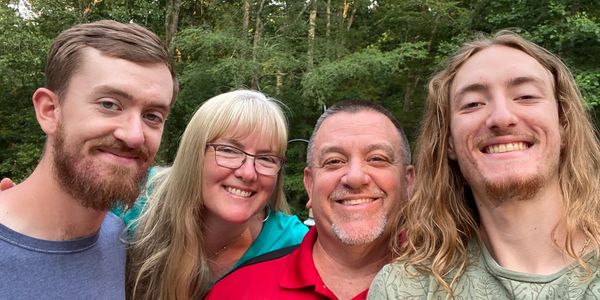 A happy family of four posing outdoors with trees in the background.