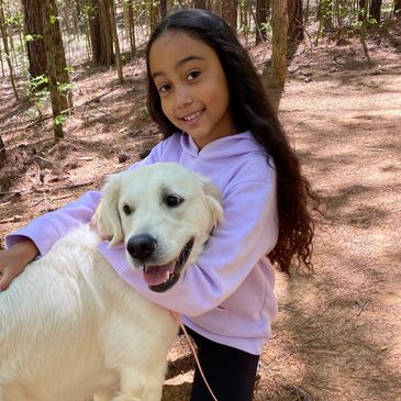 Young girl hugging a happy golden retriever in a forest.