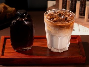 Iced coffee and syrup bottle on a wooden tray.